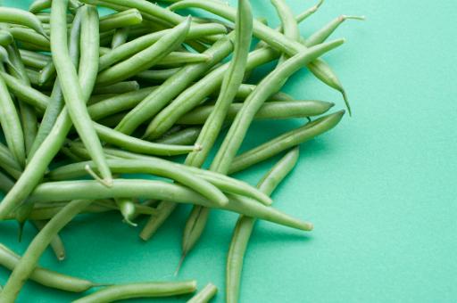 Pile of healthy fresh green haricot beans for vegetarian cuisine or to be cooked as an accompanying vegetable to a meal on a green background