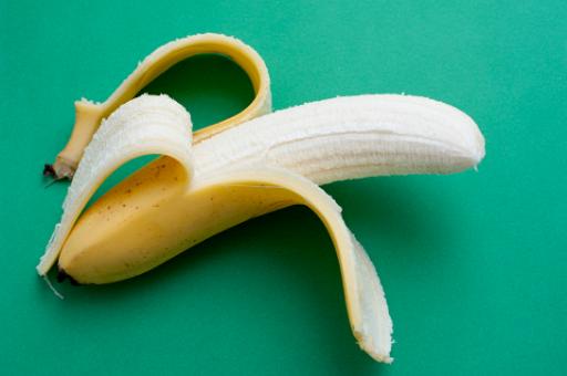 Partially peeled ripe banana showing the sweet flesh of this popular tropical fruit on a green background