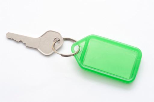 Small silver metal key attached to a blank green plastic key tag with copyspace for your text, on a white background
