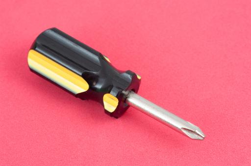 Short Phillips head screwdriver lying diagonally on a red background in a DIY, repair and construction concept
