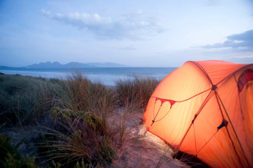 Camping tent pitched overlooking a distant marine bay illuminated at night from inside glowing in the evening light with copyspace