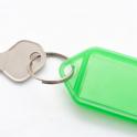 Small silver metal key attached to a blank green plastic key tag with copyspace for your text, on a white background