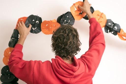 Person hanging paper garlands for Halloween with orange and black pumpkin faces on a white wall at home