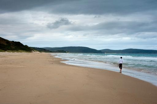 Person taking a lone beach walk alongside the surf on a deserted sandy beach on a cold overcast day, scenic view with copyspace