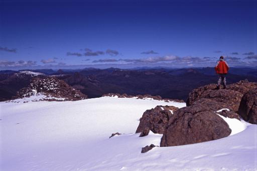 Mountain view in winter with a lone man standing on rocks above a layer of fresh snow looking out across distant mountain ranges and peaks enjoying the scenic beauty of nature