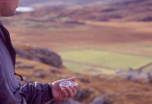 Wilderness navigation with a partial closeup view of a man holding a magnetic compass showing him the direction of magnetic north so that he can navigate to his destination